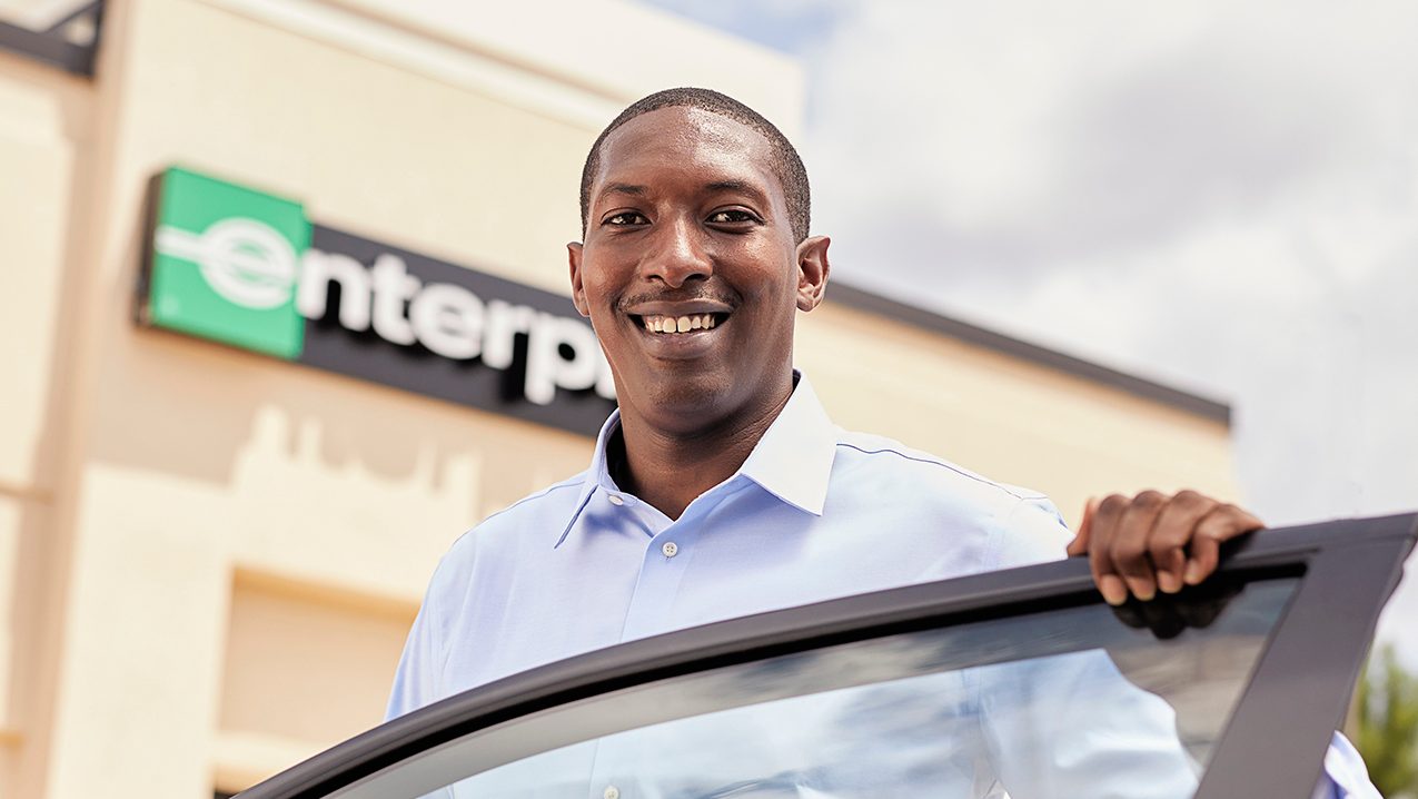 Team member smiling while leaning over an open car door 