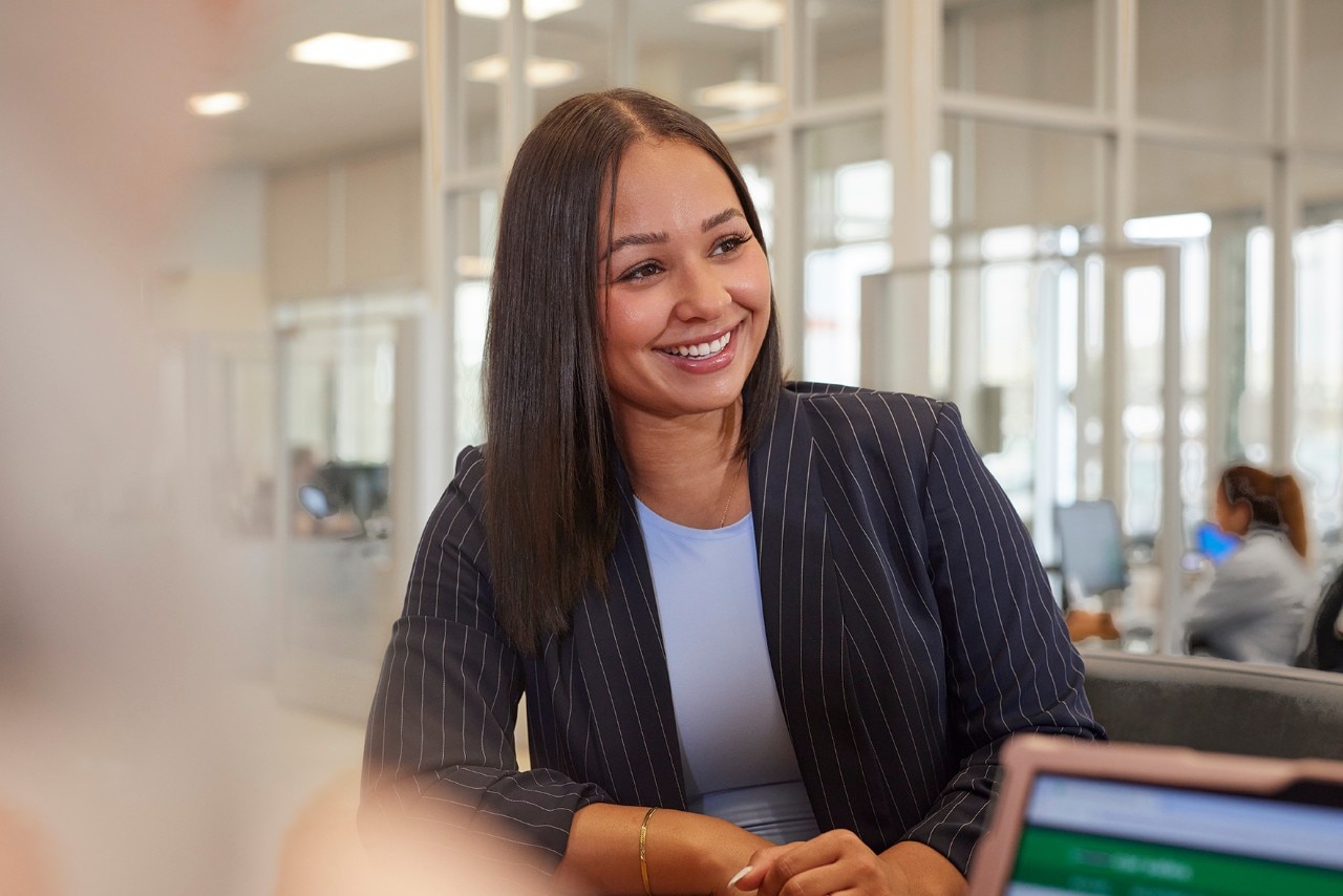 Enterprise Mobility team member sitting at a desk smiling at the person sitting next to them. 