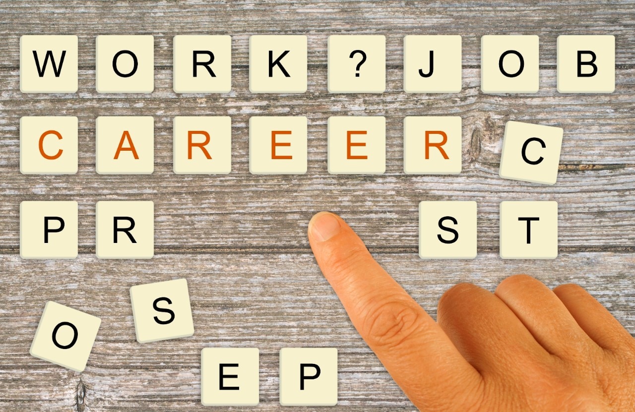 Letter tiles being arranged by a finger to spell "work", "job", "career" and then extra tiles scattered about