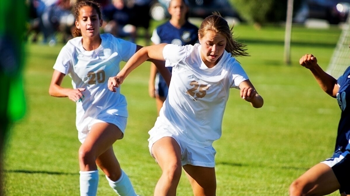 Girls playing soccer in white uniforms