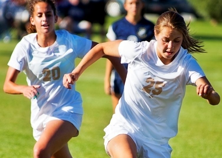 Girls playing soccer in white uniforms