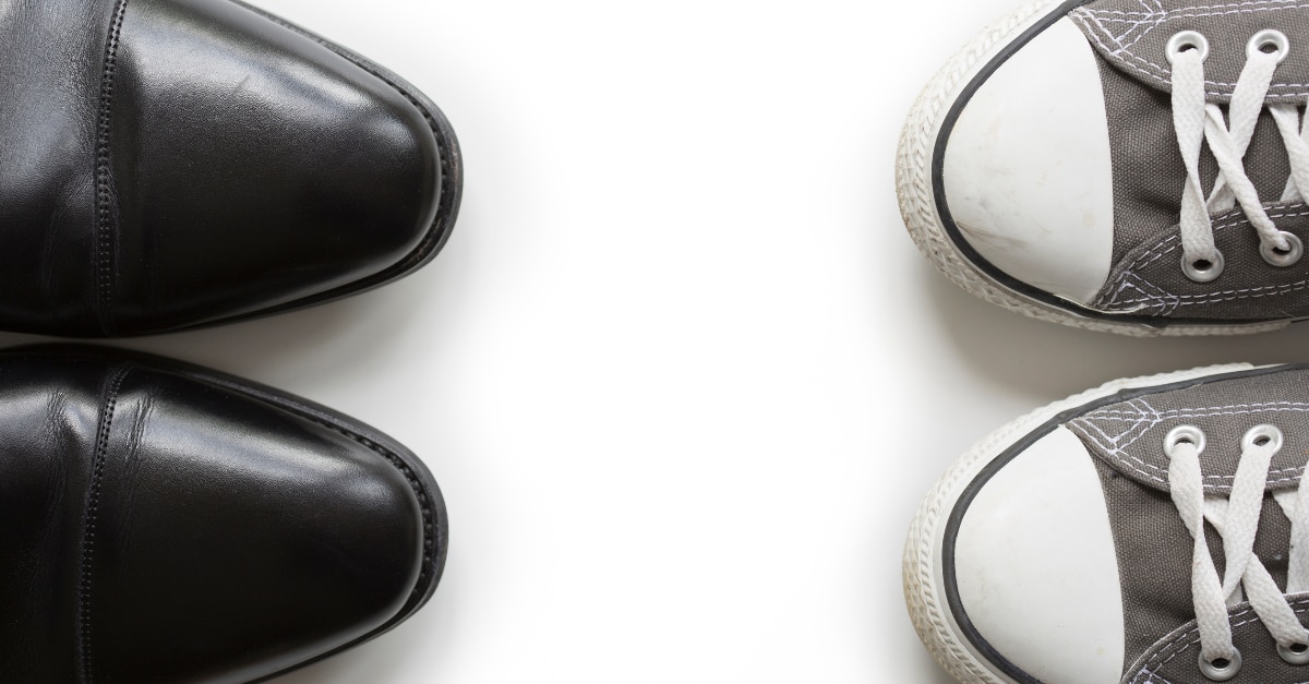 Pair of black dress shoes facing a pair of grey converse