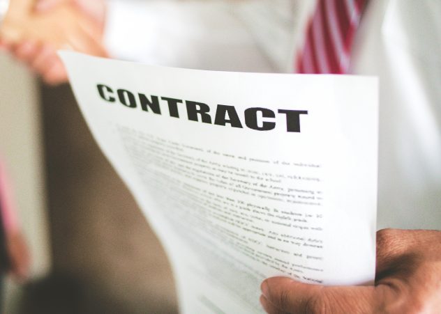 Blurred people shaking hands with a paper that says "Contract" in focus