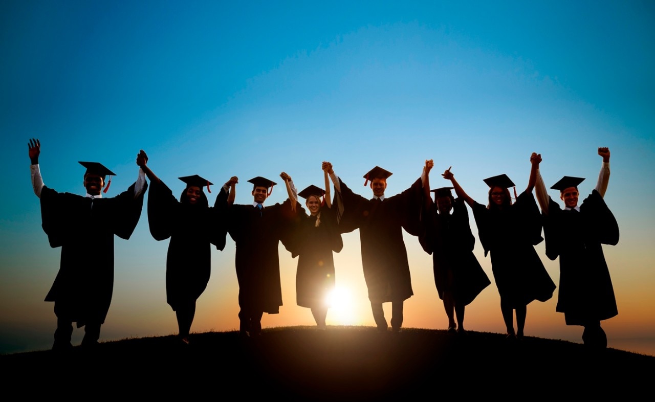 Students in graduation caps and gowns walking into the sunset