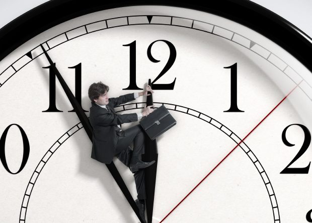 A man with a briefcase riding the hour hand of a clock
