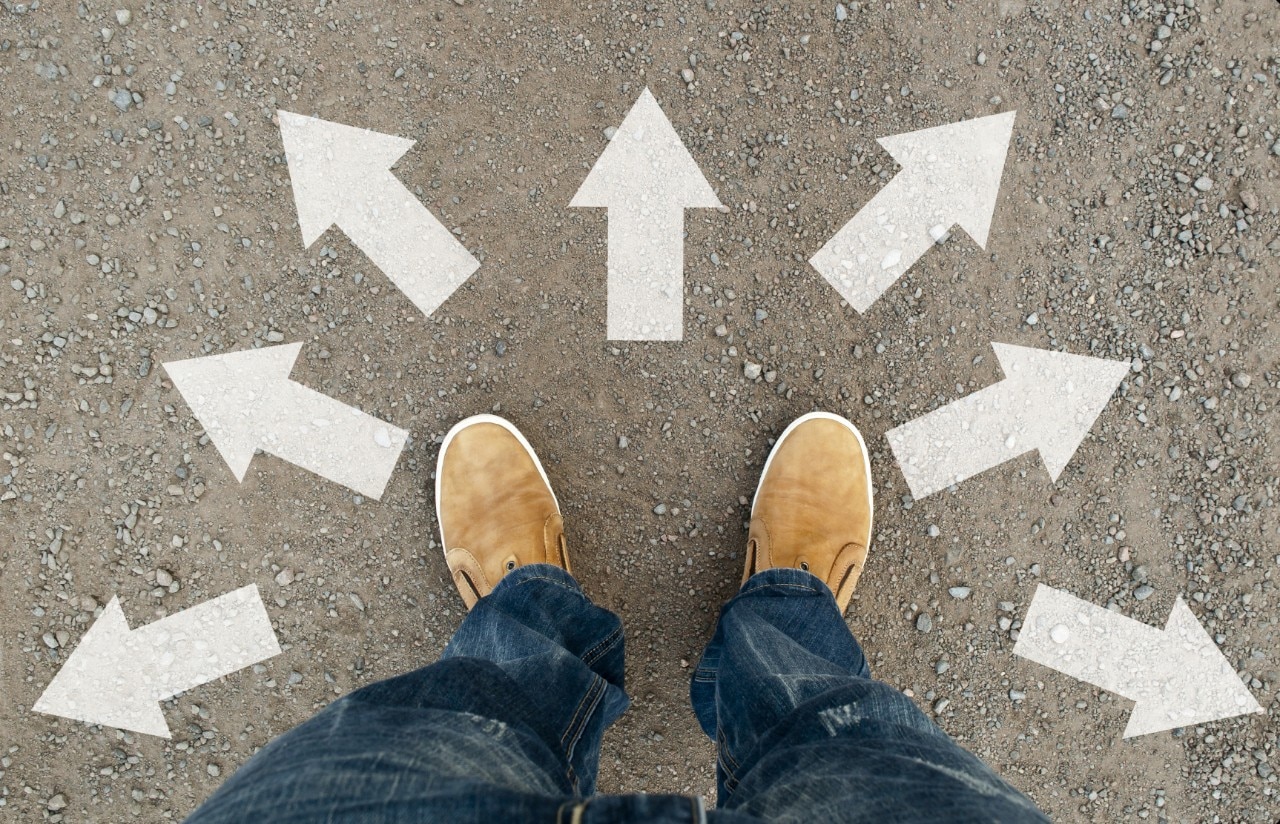 Feet with tan shoes on pavement with arrows pointing in multiple directions