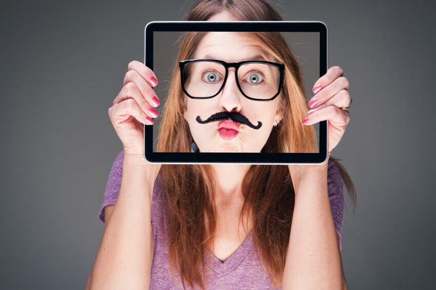 Girl holding iPad in front of her face with a picture of her face with a fake mustache and glasses