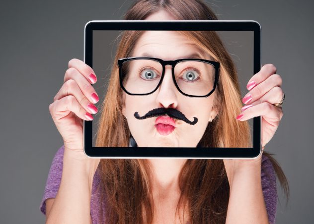 Girl holding iPad in front of her face with a picture of her face with a fake mustache and glasses