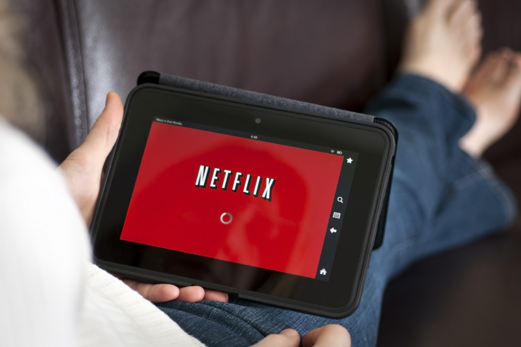 Tablet with Netflix on it held by person sittin on couch with legs crossed